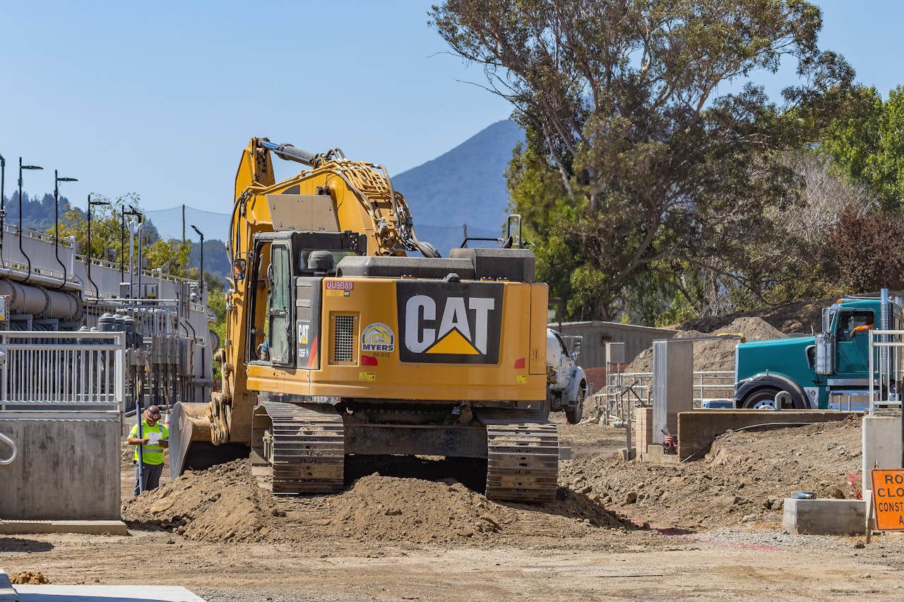 Excavator working at a construction site with mountains in the background.