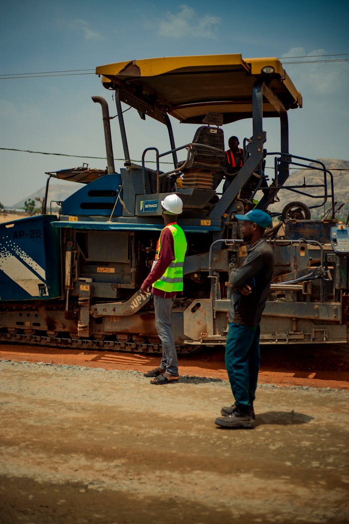 our-experience Two construction workers observing roadwork machinery under bright daylight.