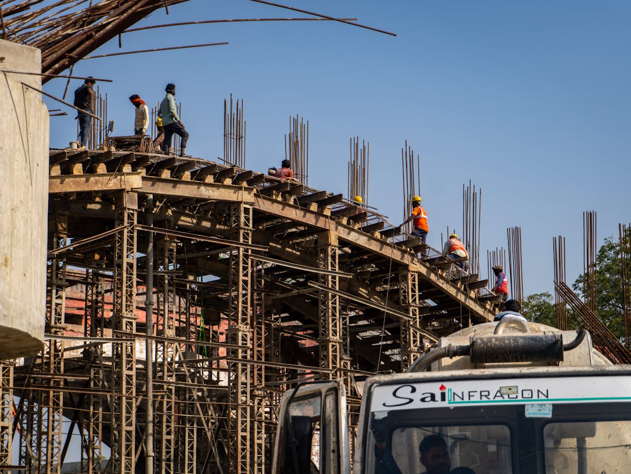 Workers construct a large industrial structure under clear blue skies, wearing safety gear.