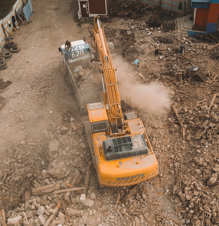 services-01 Aerial view of an excavator loading debris at a construction site with workers nearby.